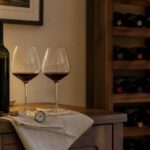 Botella de vino sin etiqueta, dos copas y termómetro junto a un botellero doméstico